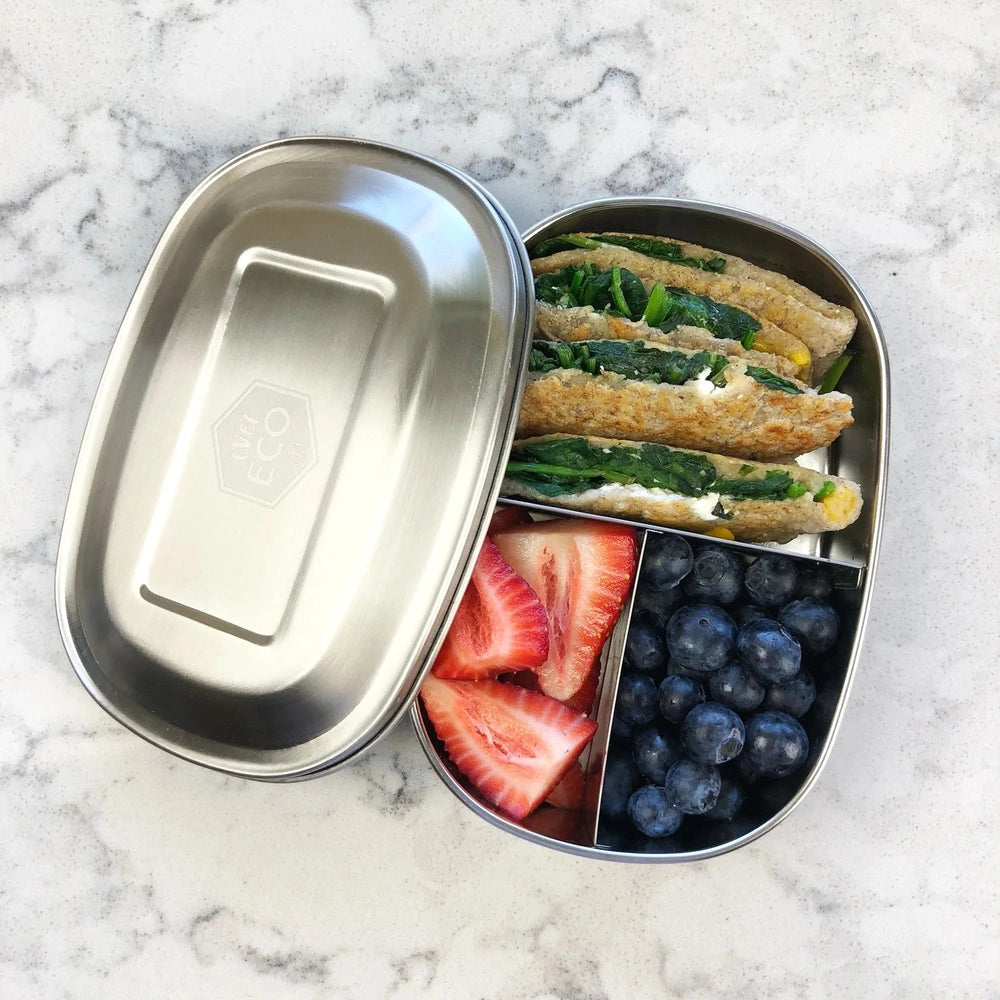 Stainless Steel  lunch box with 3 compartments containing sandwiches, strawberries, and blueberries on a marble surface.