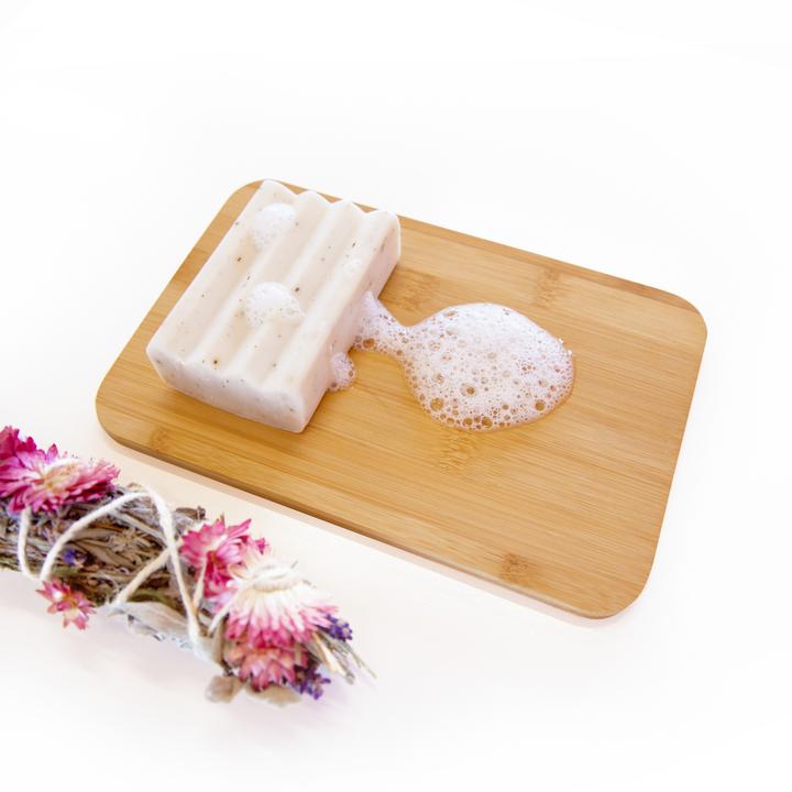 Bar of Hannah Pad Probiotic Laundry Soap Wooden Board next to Dried Flowers.