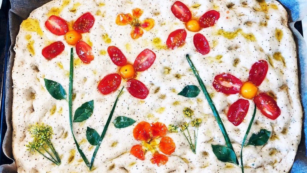 Uncooked focaccia with toppings arranged into flower patterns
