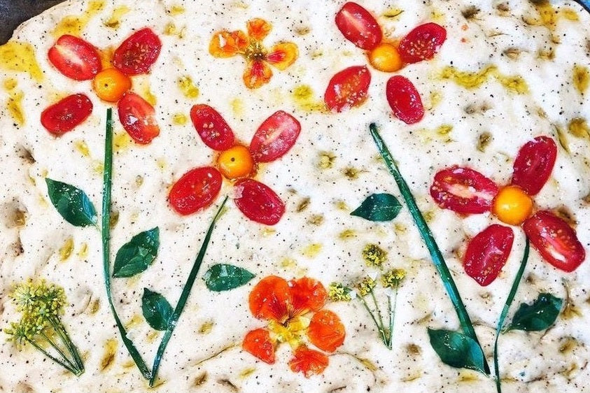 Uncooked focaccia with toppings arranged into flower patterns