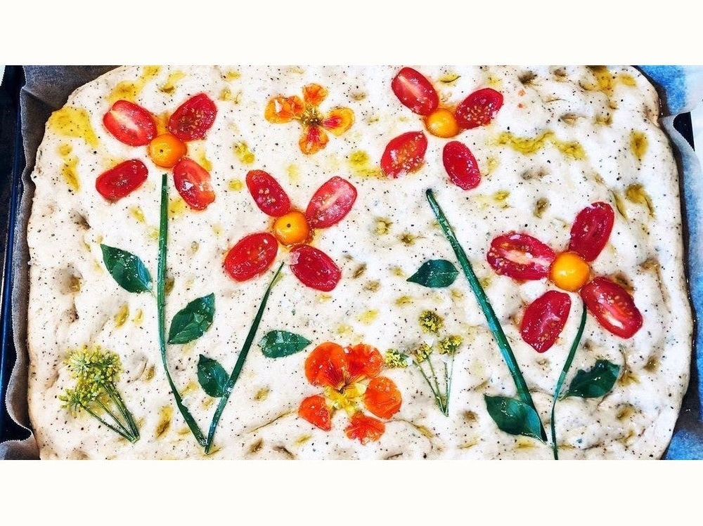 Uncooked focaccia with toppings arranged into flower patterns