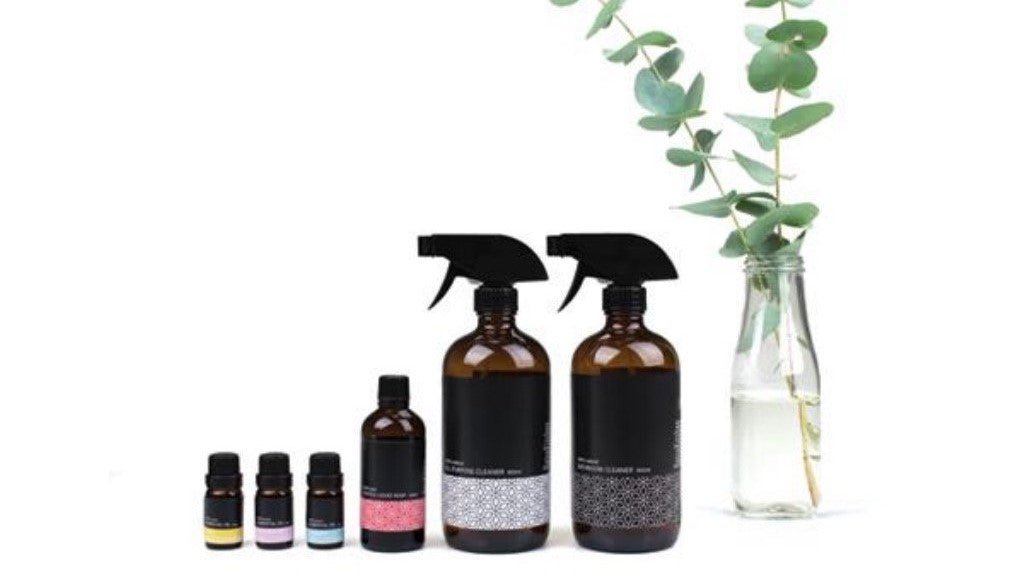 Make your own natural cleaning kit ingredients lined up including essential oils and reusable glass spray bottles