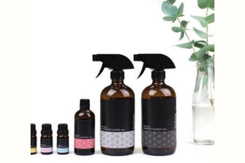 Make your own natural cleaning kit ingredients lined up including essential oils and reusable glass spray bottles