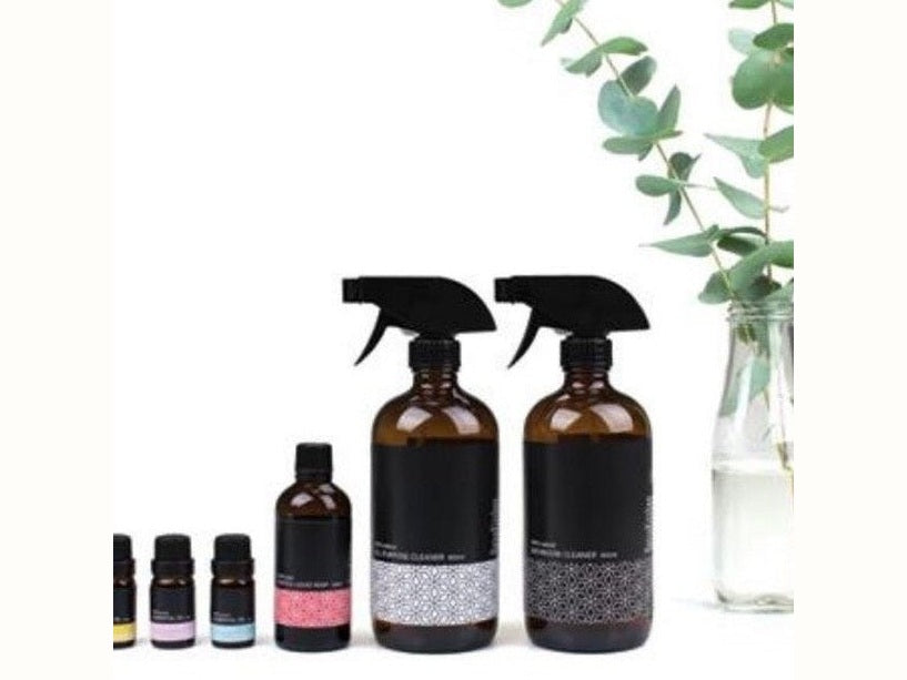 Make your own natural cleaning kit ingredients lined up including essential oils and reusable glass spray bottles
