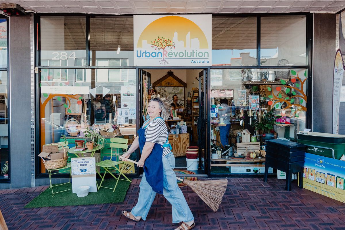 Bec riding a broom stick at the front of Urban Revolution eco store in Victoria Park