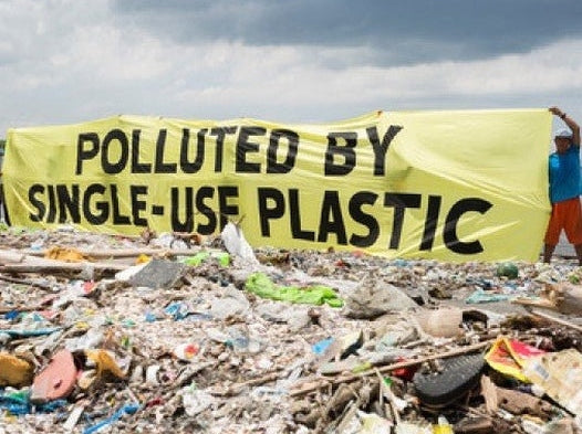 Polluted By Single-Use Plastic Sign on a shore behind beached plastic waste