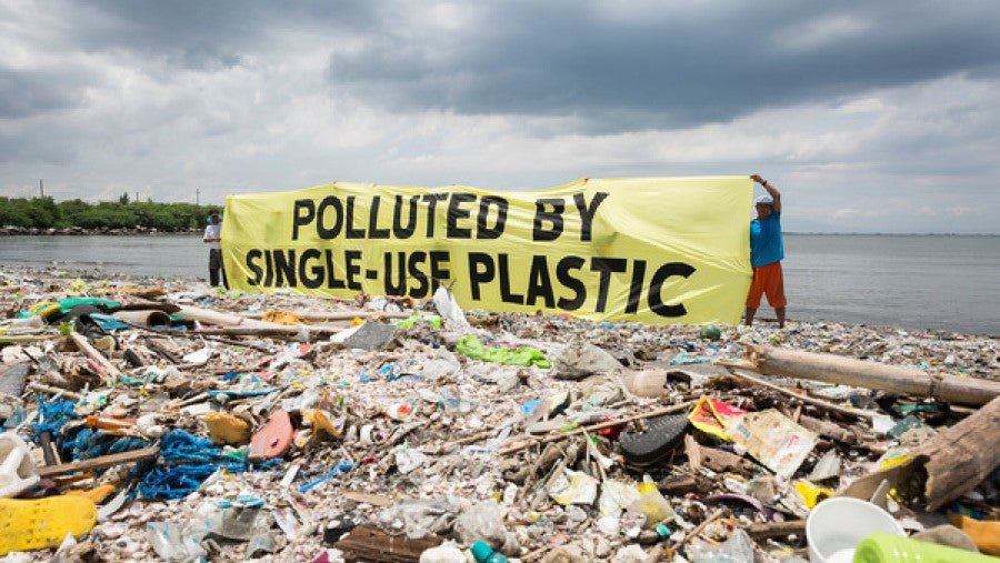 Polluted By Single-Use Plastic Sign on a shore behind beached plastic waste