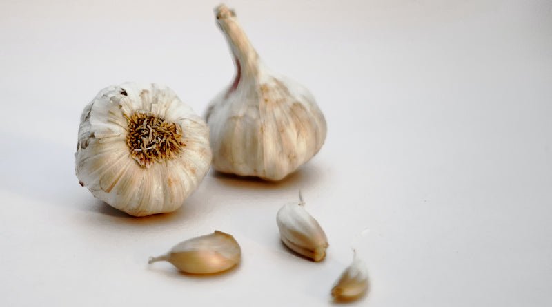 Two bulbs of garlic with three loose cloves on a white background
