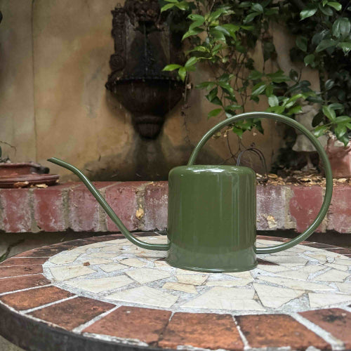 Green watering can on a mosaic patio with plants in the background