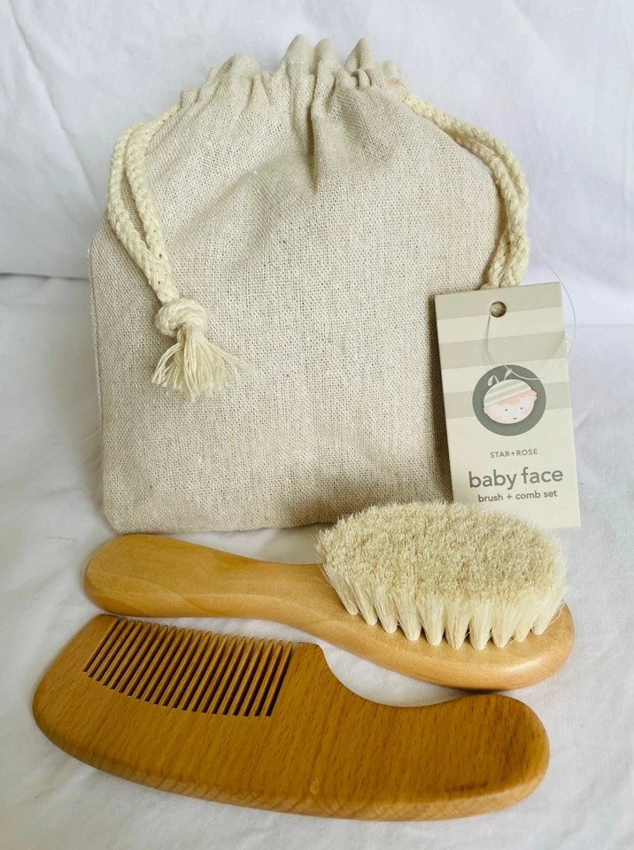 A baby grooming set that includes a wooden comb, a wooden brush with soft goats hair bristles, and a beige drawstring linen bag with baby face labelled tag from Star + Rose.