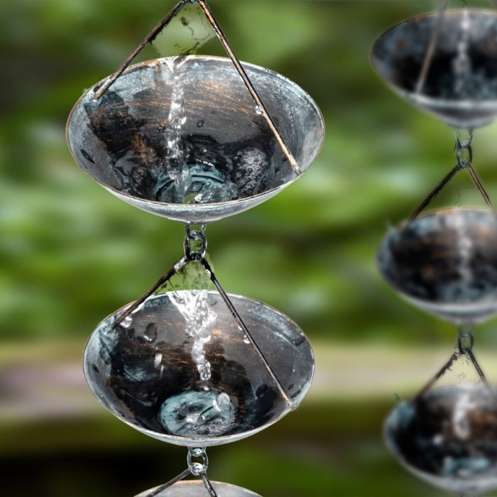 Metal Rain Chain with Water Flowing through it against a Green Background.