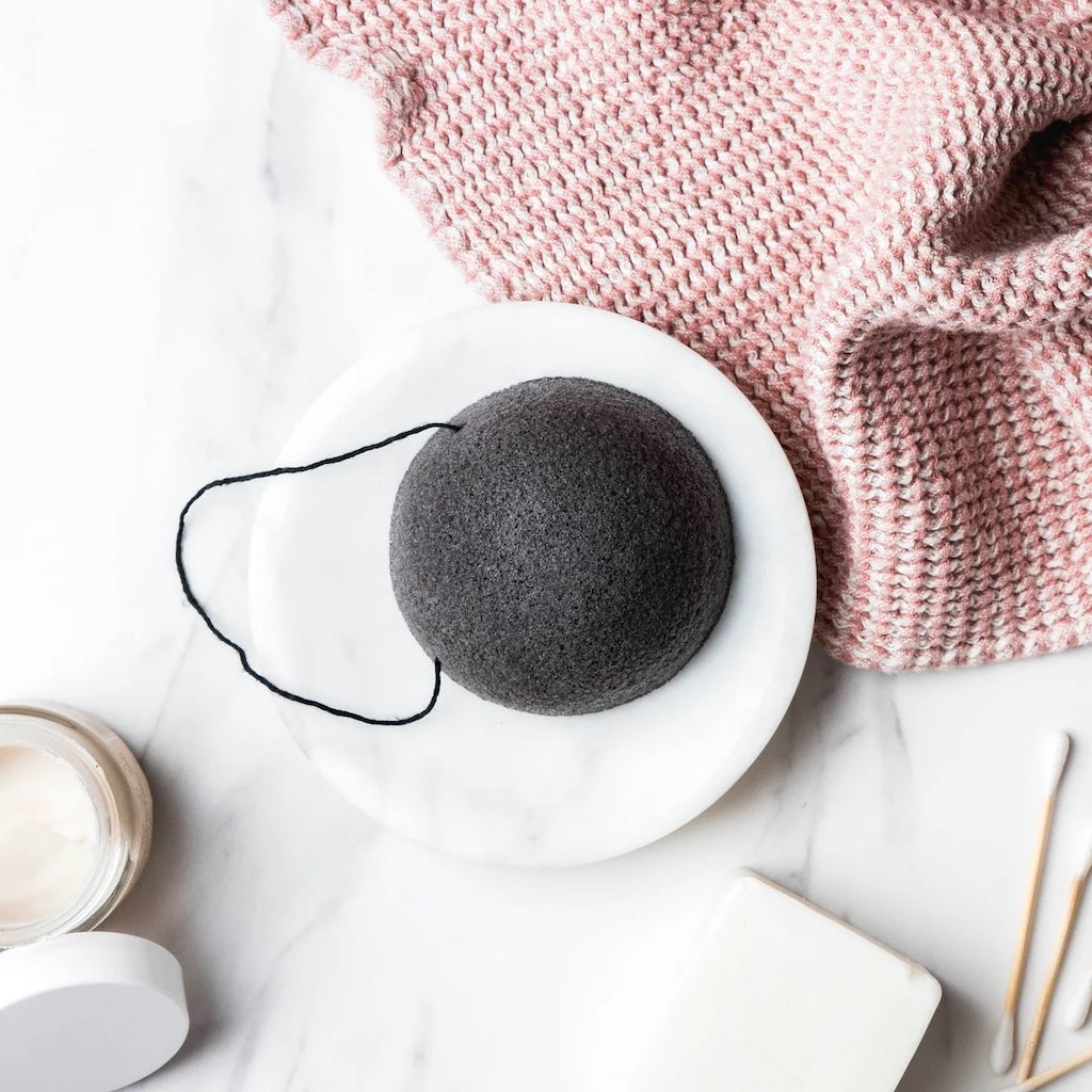 Charcoal infused konjac sponge with cotton hanging loop displayed on a white plate