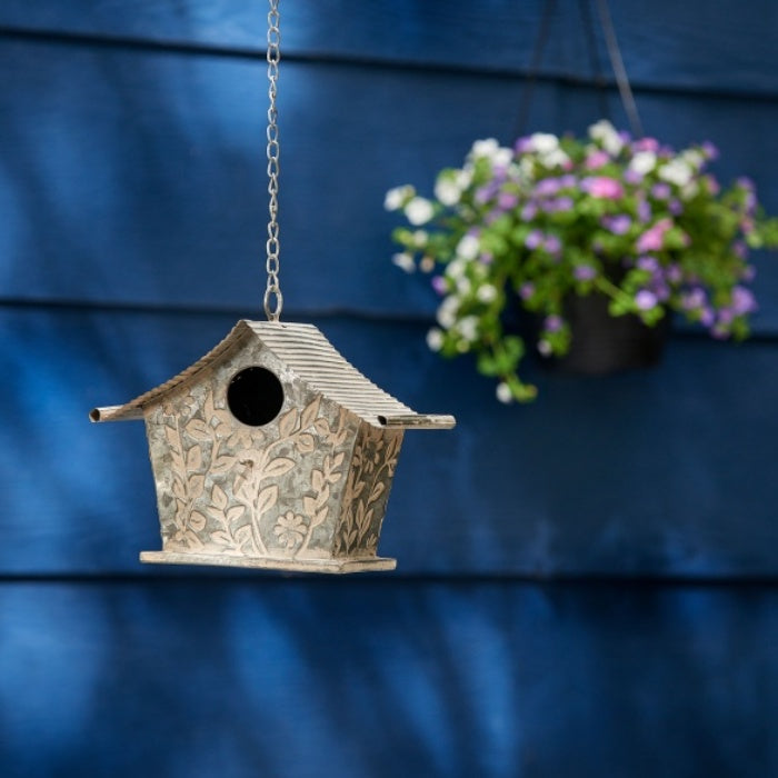Decorative Birdhouse Hanging against a Blue Wall with a Potted Plant in the Background.