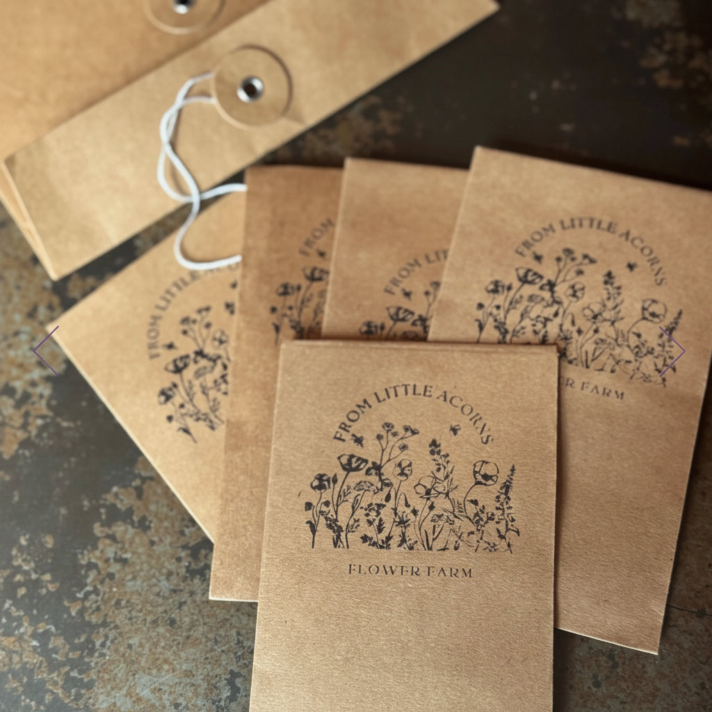 Brown paper seed packets with 'From Little Acorns Flower Farm' branding on a textured surface.