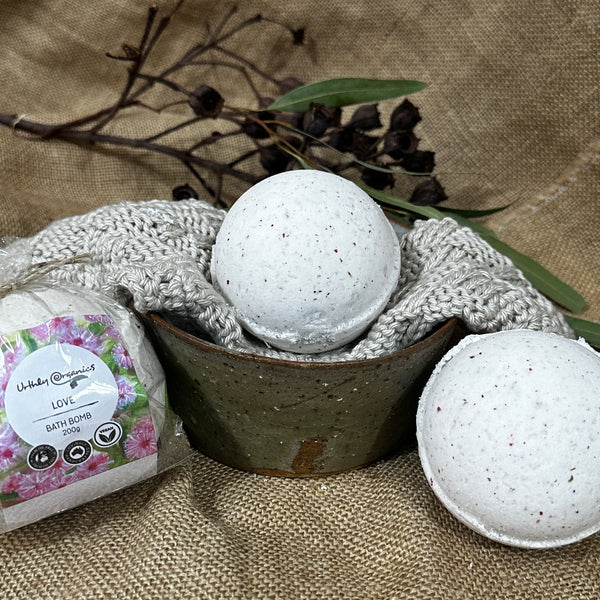 Three Love bath bombs, one wrapped with pink flower packaging and two unwrapped