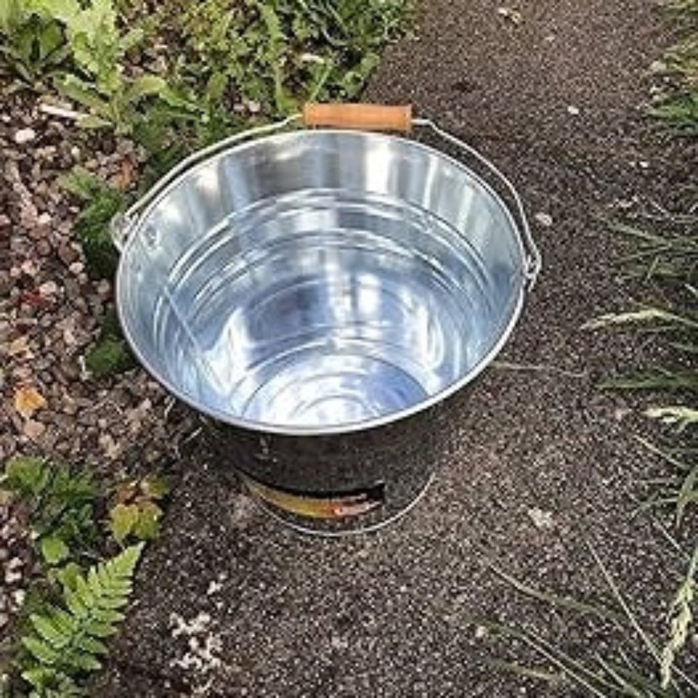 Metal bucket on a concrete surface with grass and leaves in the background