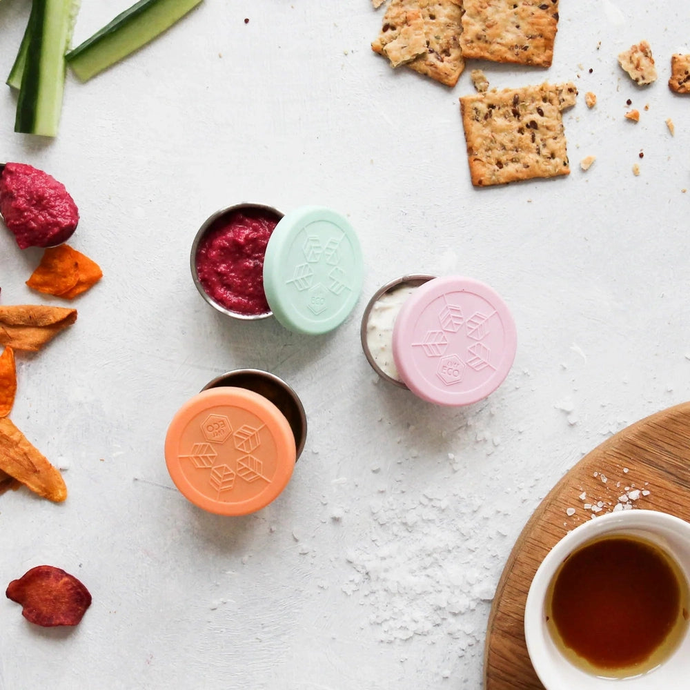 Colourful containers with lids on a table with crackers and a cup of tea.