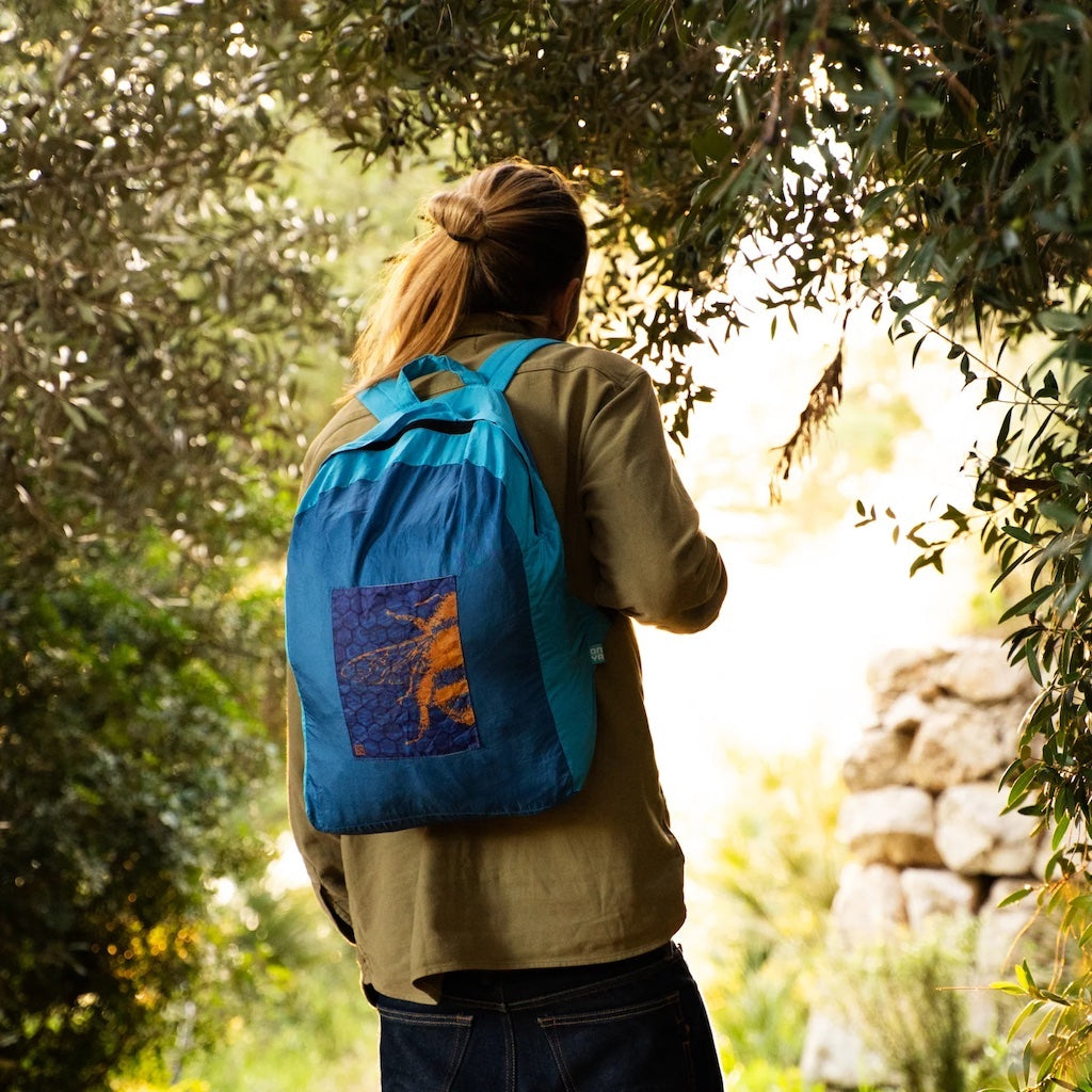 Man wearing Onya turquoise and teal coloured backpack with Bee Hive design in a forest setting.