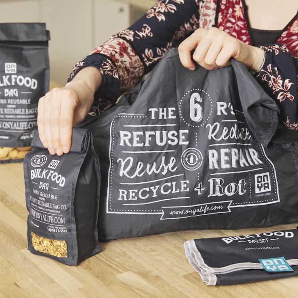 Woman holding a set of Onya reusable bulk food bags in charcoal colour with the 6 R's artwork on the front.