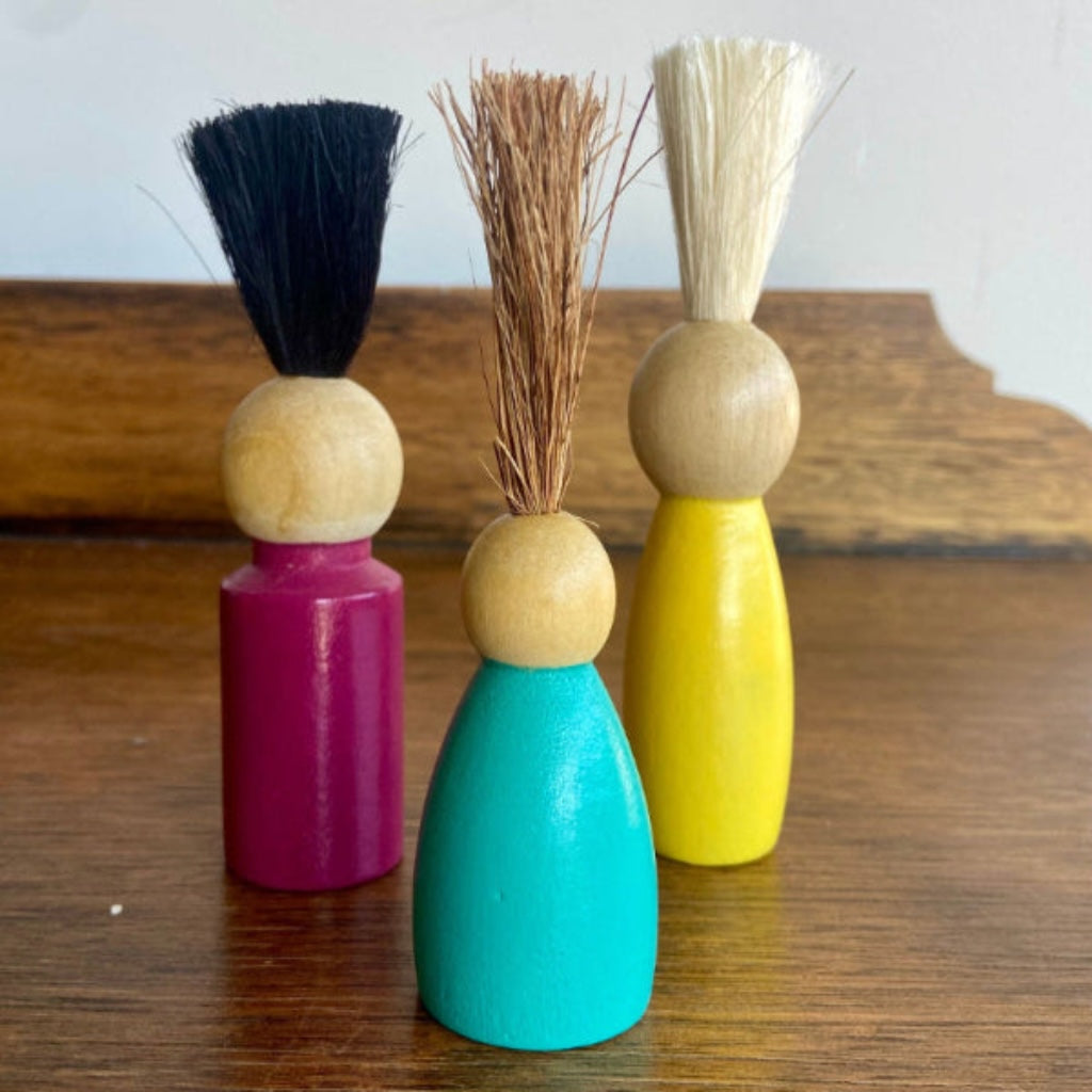 Three wooden brushes with colorful handles on a wooden surface.