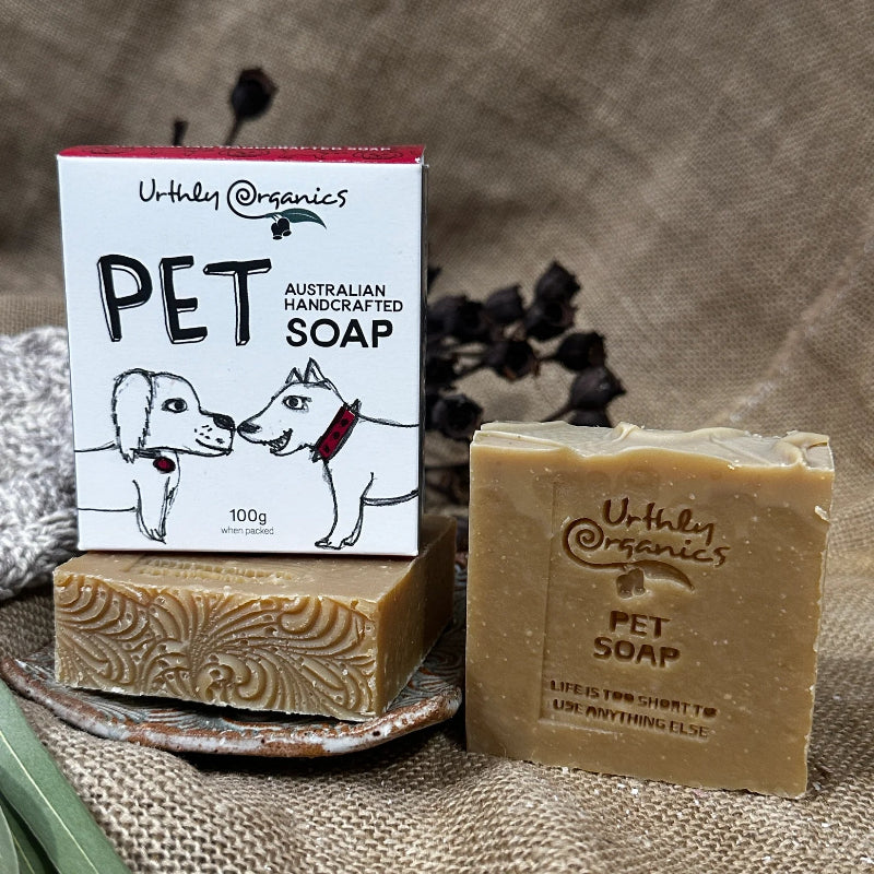 Two Bars of Urthly Organics Pet Soap with Packaging on a Textured Surface.