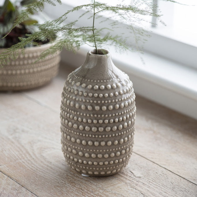 Decorative ceramic vase with textured surface on a wooden surface near a window.