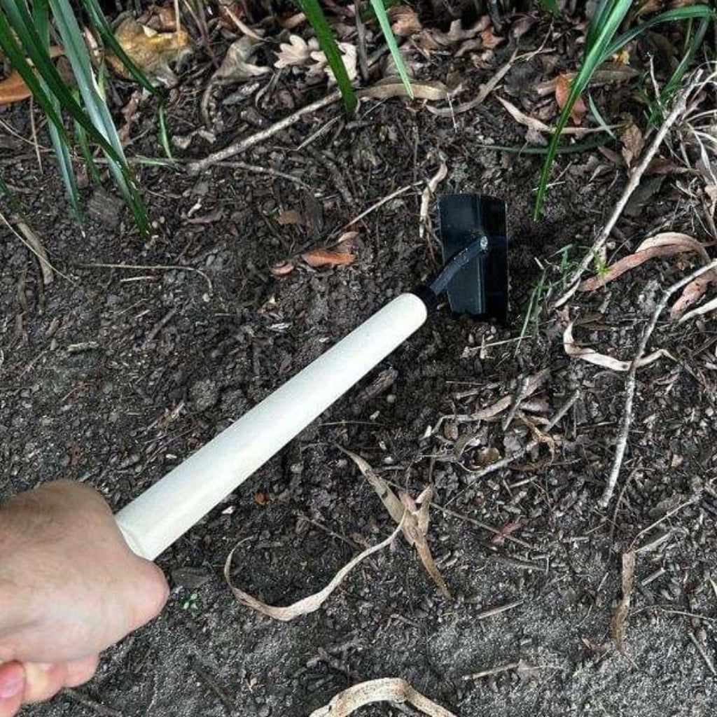Hand holding a small gardening tool in soil with green plants