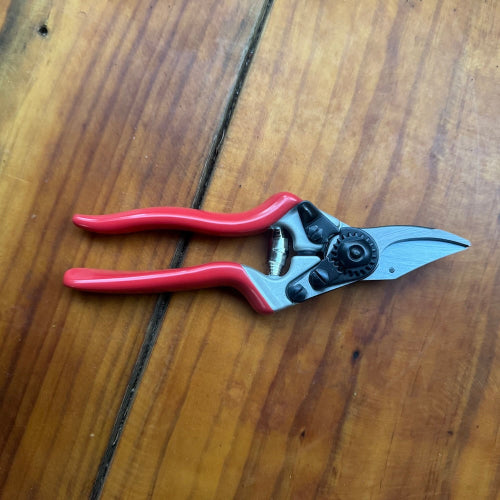 Red-handled pruning shears on a wooden surface displaying the blade lock side