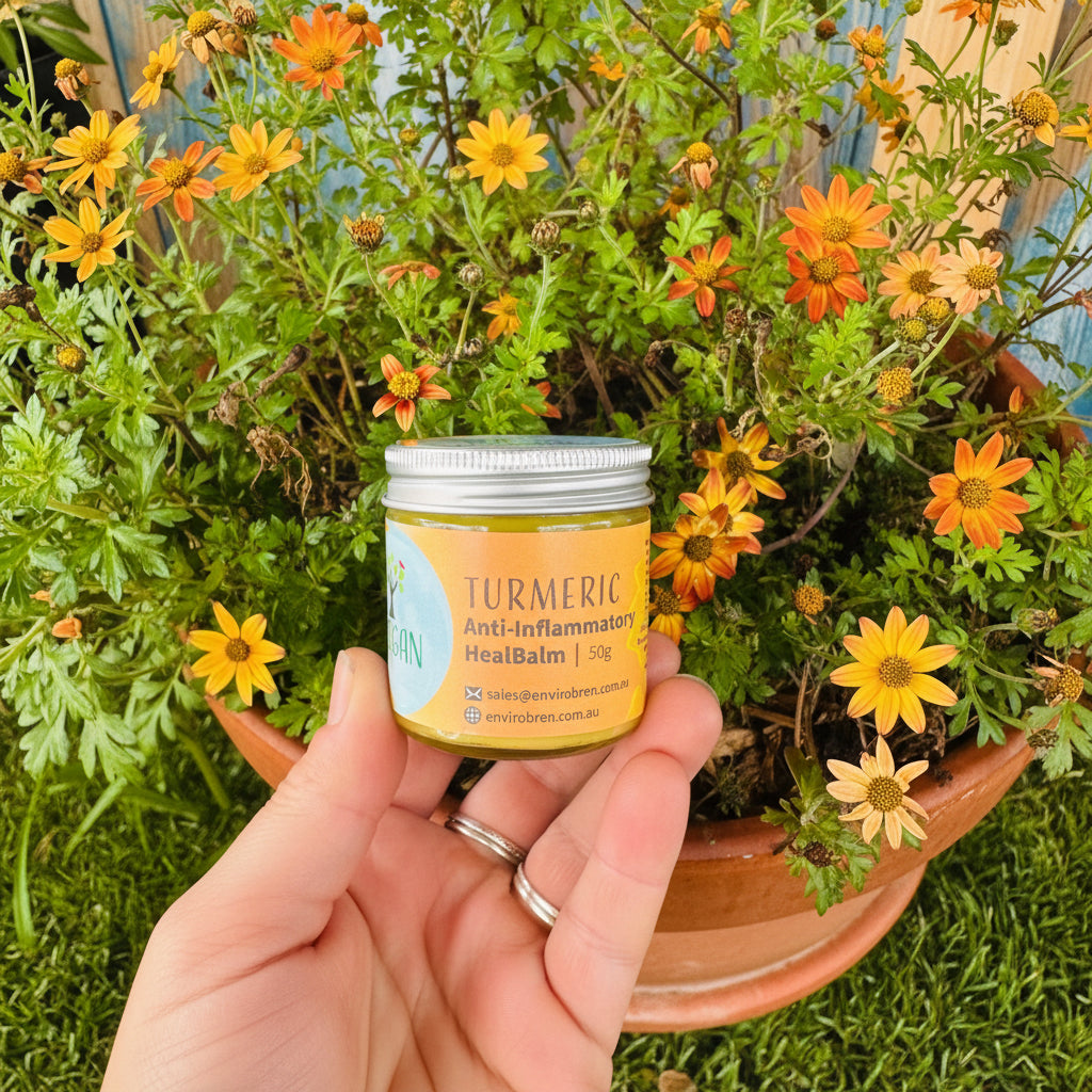 Jar of Tumeric Anti-Inflammatory Heal Balm by EnviroBren being held in front of Orange Flowers.
