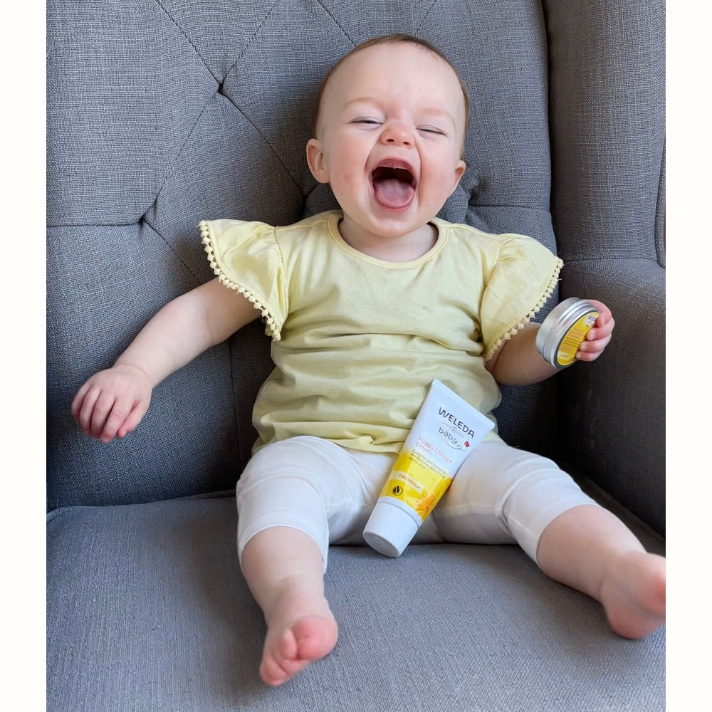 Happy baby holding a range of Weleda Baby Products
