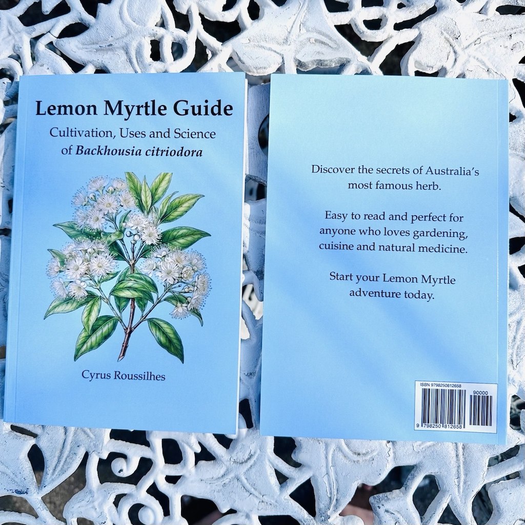 Blue-coloured book titled 'Lemon Myrtle Guide: Cultivation, Uses and Science of Backhousia citriodora' by Cyrus Roussilhes on a white decorative table.