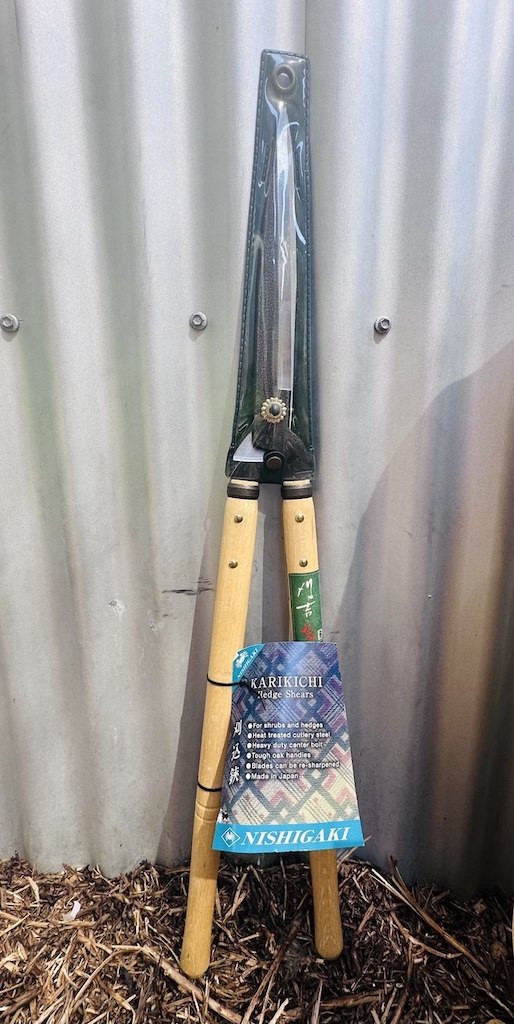 Long handled hedge shears with wooden handles and long steel blades leaning against a wall.