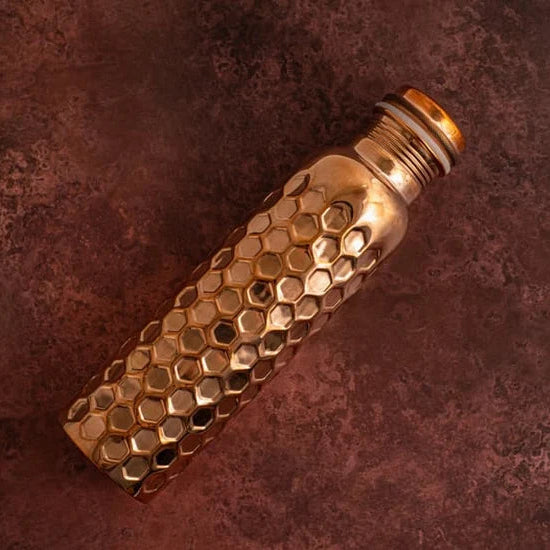 A hammered pure copper bottle with a diamond textured body and a screw on lid resting on a dark red background.
