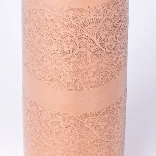 A close up of the body of a copper water bottle with intricate hand-carved floral and scroll details, shown against a plain white background.
