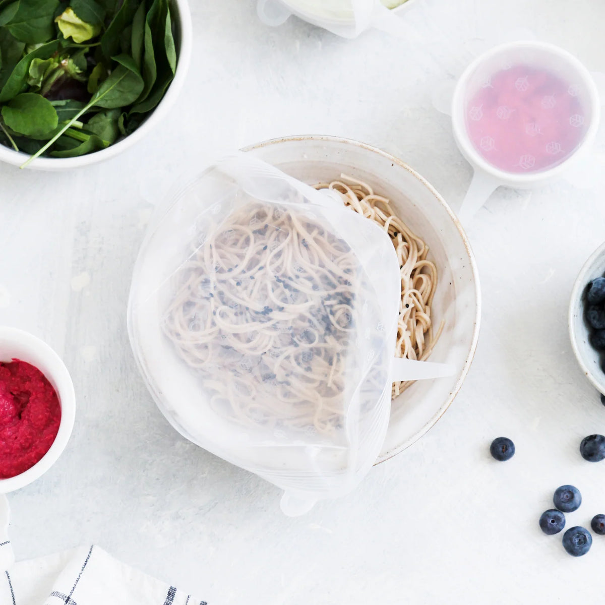 A silicone food cover is peeling back from a bowl of noodles
