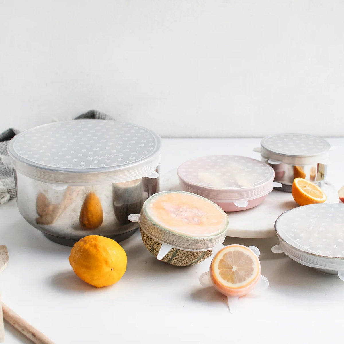 A set of silicone food covers are used to cover a bowl and some fresh fruit.