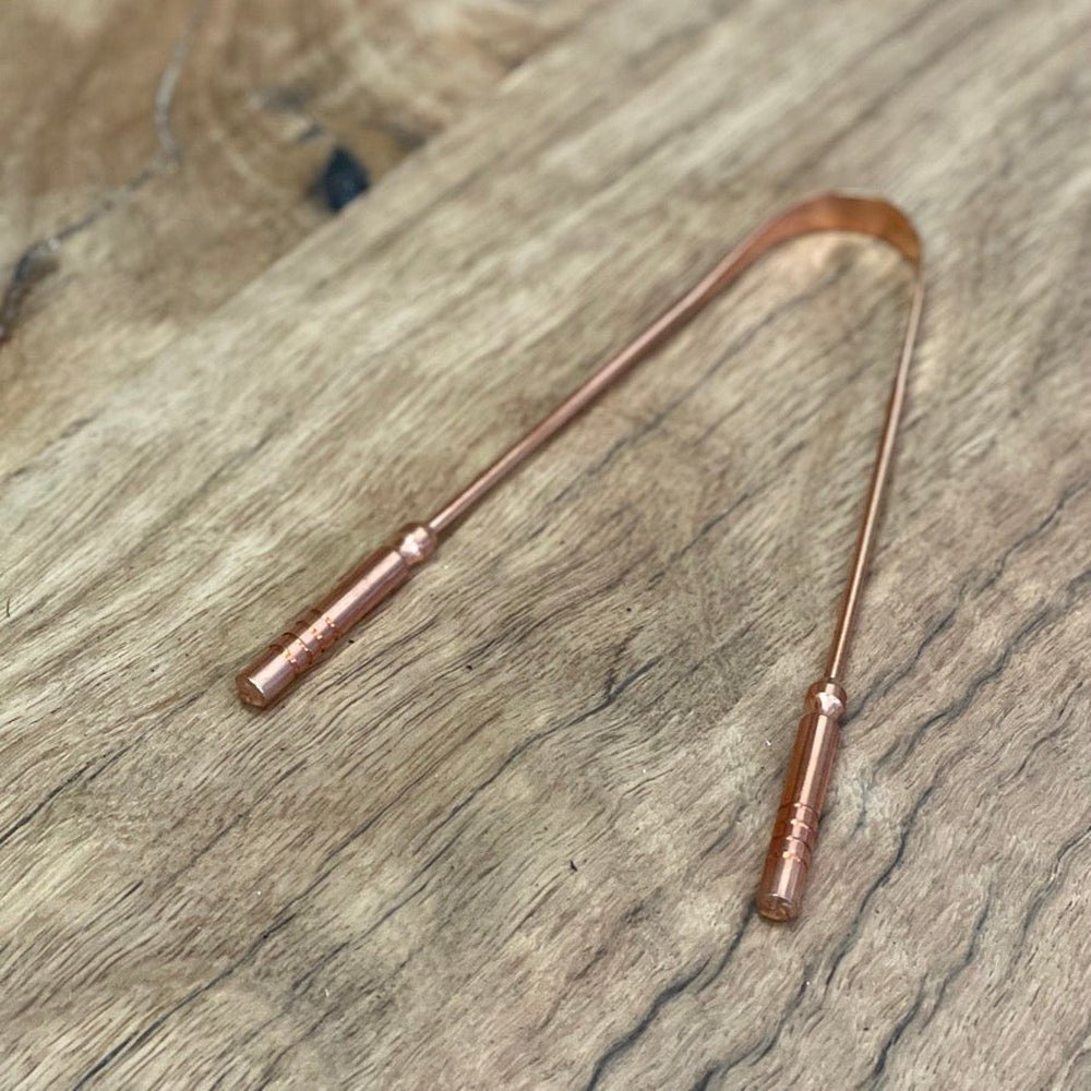 Copper tongue scraper on wooden bench